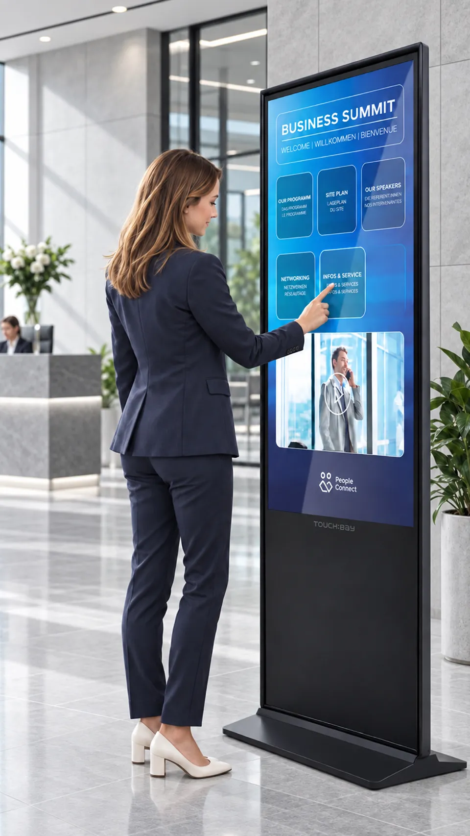 261005_Business_Header_960x1706px_V3 Touch:Bay - Geschäftsfrau steht an einer Stele in einem Foyer und guckt sich das Program einer Veranstaltung an